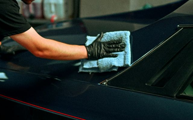 gloved hand drying a dark car with a microfiber towel