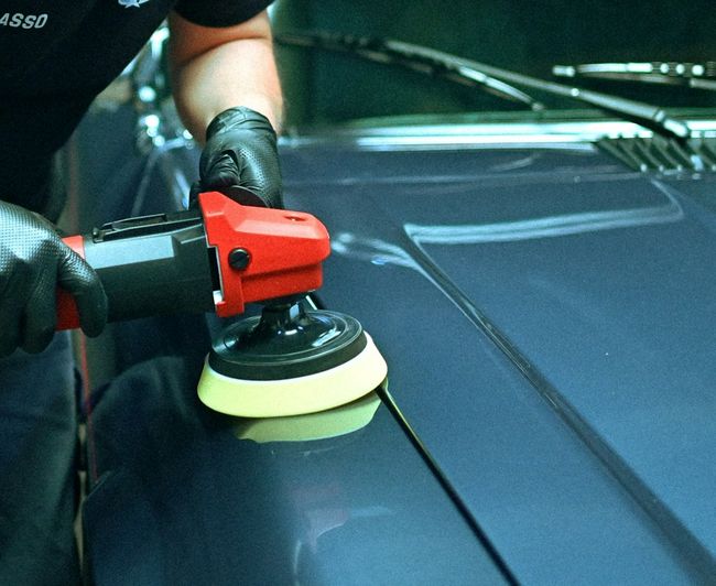detailer machine polishing a blue car hood to a mirror finish